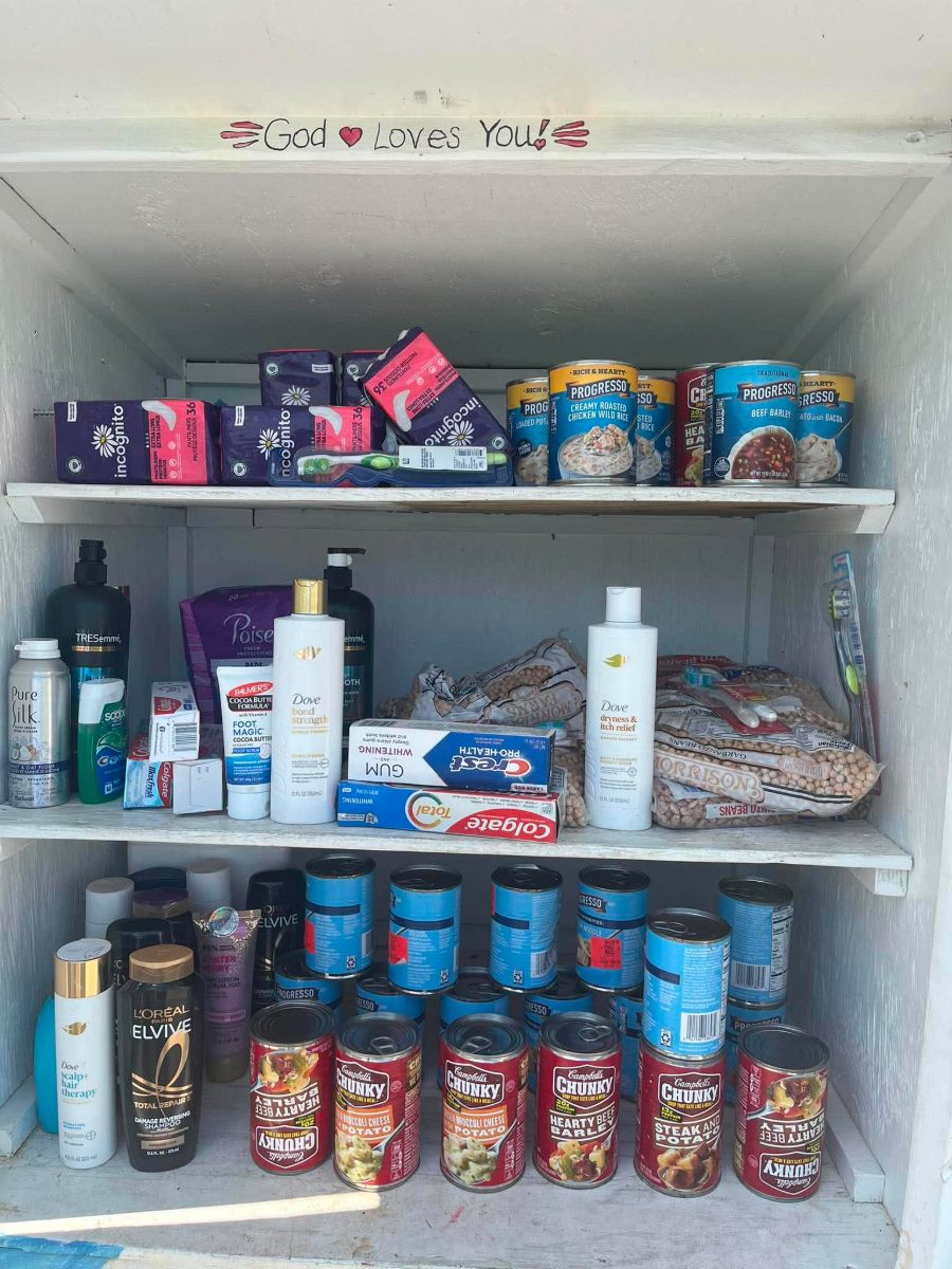 Lily's Blessing Box fully stocked with canned soup, pantry staples and hygiene items under a hand-painted God Loves You sign